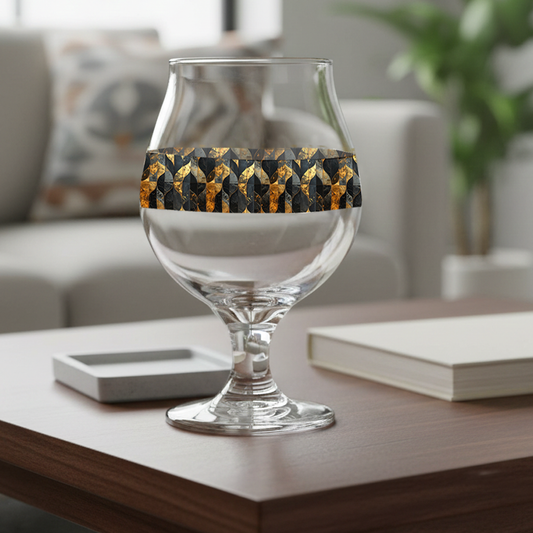Aged Elegance Belgian beer glass with a black and bronze geometric design on a wood coffee table with book, and a sofa in the backround