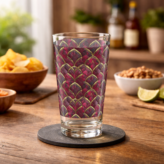 Crimson Jewels pint beer glass with ruby and gold design on a wood table with chips and nuts and bottles blurred in the background