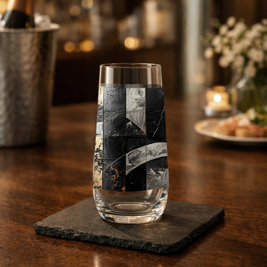 Fresco Fragments stemless champagne glass with black, silver and gold pattern on wood table with a champagne bucket and a blurred home bar in background