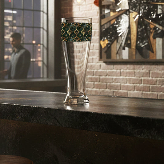 Malachite Enigma pilsner beer glass with a 360° full wrap design sitting on a bar counter in a modern lounge.