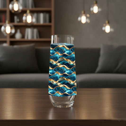 Opulent Teal stemless champagne flute glass with teal and gold wave design on a coffee table with modern sofa, lights and bookcases in background