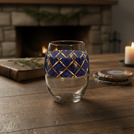 Regal Twilight stemless wine glass with sapphire and gold pattern on a wooden table with a fireplace in the background