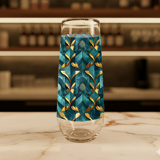 Gilded Patina stemless champagne flute glass with teal and gold geometric pattern on a marble surface with blurred background