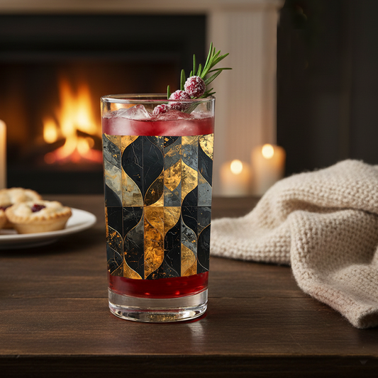 Aged Elegance highball glass of cocktail with charcoal and bronze decorative design on a table in front of a fireplace with candles and a throw.