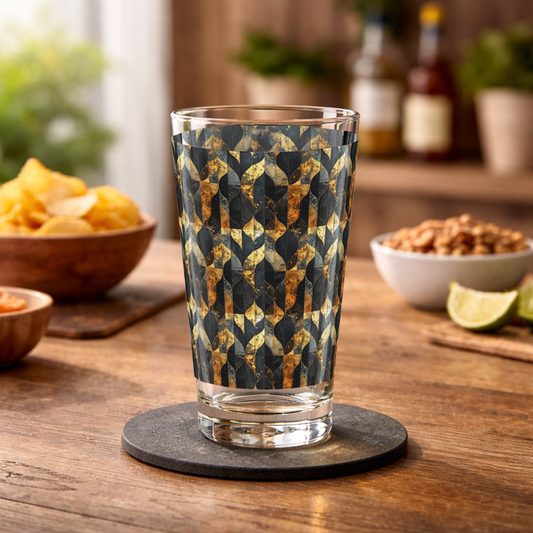 Aged Elegance charcoal and bronze pattern pint beer glass on a wood table with chips and nuts and a blurred counter with plants in background