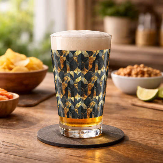 Aged Elegance charcoal and bronze pattern pint glass filled with beer and foam head on a wood table with chips and nuts and a blurred counter with plants in background
