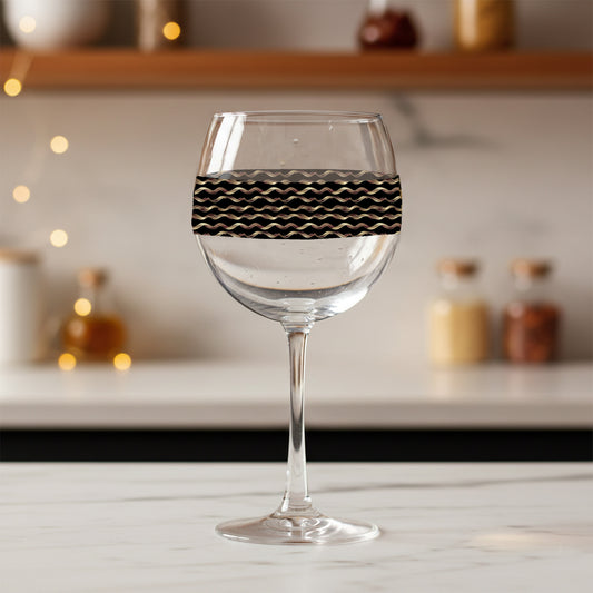Liquid Gold balloon wine glass with black and gold wavy design on a blurred kitchen background