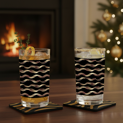 Two Liquid Gold highball glasses in a black and gold wavy design with drinks on a table in front of a fireplace and Christmas tree.