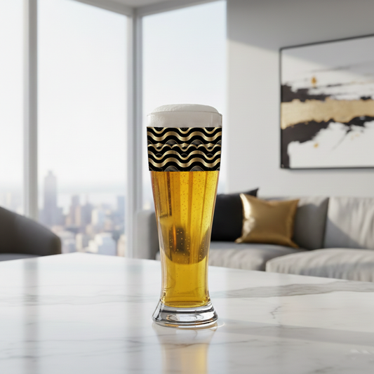 Liquid Gold pilsner beer glass with a black and gold wave design filled with f beer on a marble surface in a modern living room.