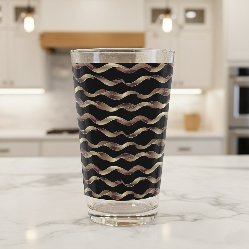 Liquid Gold pint beer glass with gold and black wavy design on a marble kitchen counter with blurred background.