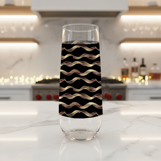 Liquid Gold stemless champagne glass with black and gold wavy design on a marble kitchen counter with blurred background.