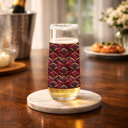 Crimson Jewels stemless champagne glass with a ruby and gold design on a table iwith champagne bucket in background