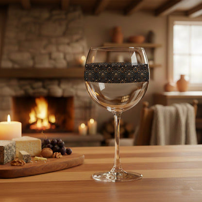 Foundry Coppers balloon wine glass with a dark ash and copper discs design and grapes, cheese and candle on a table in a cozy room with a fireplace.