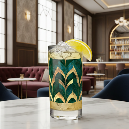 Emerald Royale highball glass with green and gold art deco design, cocktail with lemon wedge, and ice cubes on a table in a stylish bar setting.