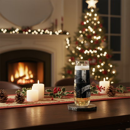 Fresco Fragments stemless champagne glass with black, silver and gold pattern on a table with a Christmas tree and fireplace in the background