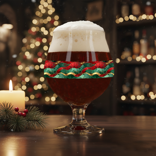 Royal Flux Belgian beer glass with dark ale and a green, red, and gold design on a table with candle and christmas tree in the background