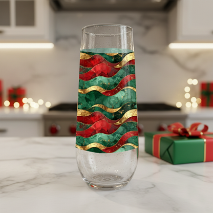 Royal Flux stemless champagne flute glass detailing red, green, and gold wavy design on a kitchen counter with a holiday gift box and blurred background.