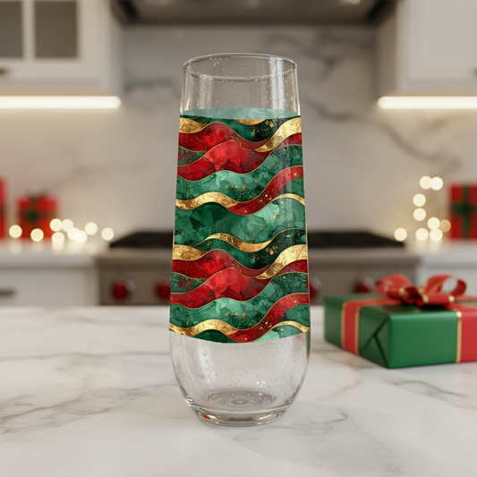Royal Flux stemless champagne flute glass detailing red, green, and gold wavy design on a kitchen counter with a holiday gift box and blurred background.