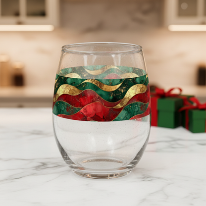 Royal Flux stemless wine glass with red, green, and gold wavy design on a marble surface with blurred gift boxes in the background.