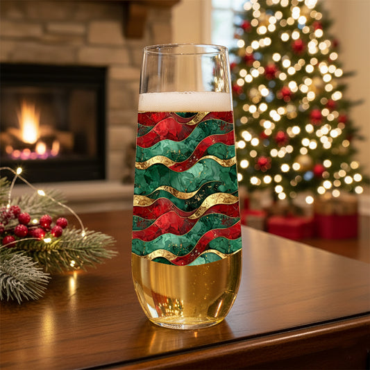 Royal Flux stemless champagne glass with red, green, and gold wavy pattern on a table with a Christmas tree and fireplace in the background.