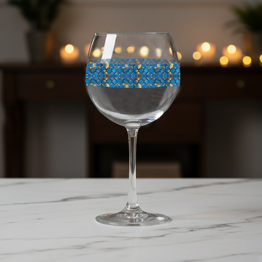 Moroccan Treasure balloon wine glass with turquoise and gold decorative design on a marble surface with blurred lights in the background