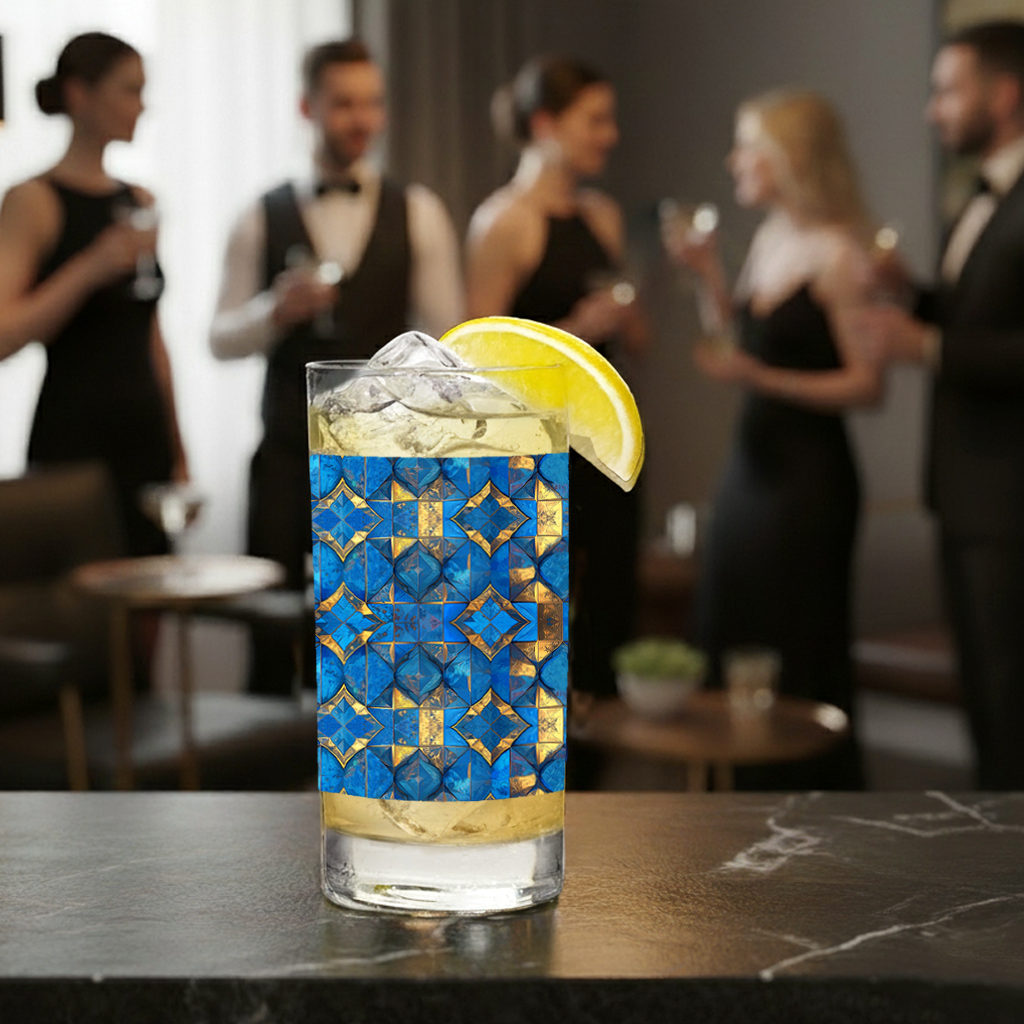 Moroccan Treasure highball glass with a turquoise and gold design, filled with a  cocktail sittihg on a bar, with people in formal attire in the background.