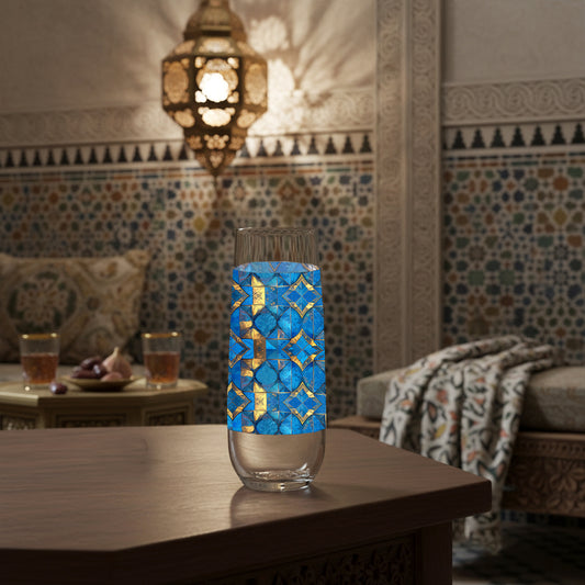 Moroccan Treasure stemless champagne glass with geometric blue and gold design sitting on a Mediterranean table with mosaic wall behind it and hanging lantern.