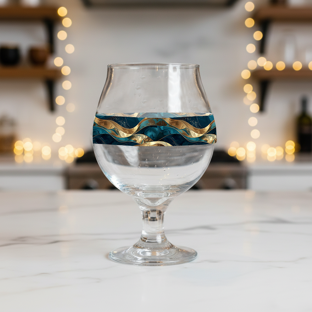 Opulent Teal Belgian beer glass with a teal and gold wave design on a kitchen counter with blurred lights in the background