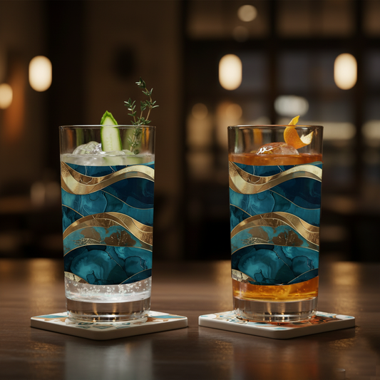 Two Opulent Teal highball glasses with a teal and gold decorative design filled with cocktails on a wooden surface and blurred backgroun.