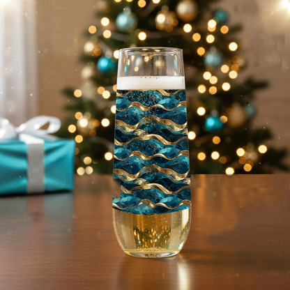 Opulent Teal stemless champagne flute glass with teal and gold decorative pattern on a table with a present in front of a Christmas tree.