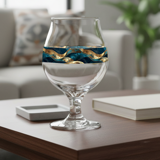 Opulent Teal Belgian beer glass with a teal and gold wave design on a coffee table with book and coaster, and a sofa blurred in background