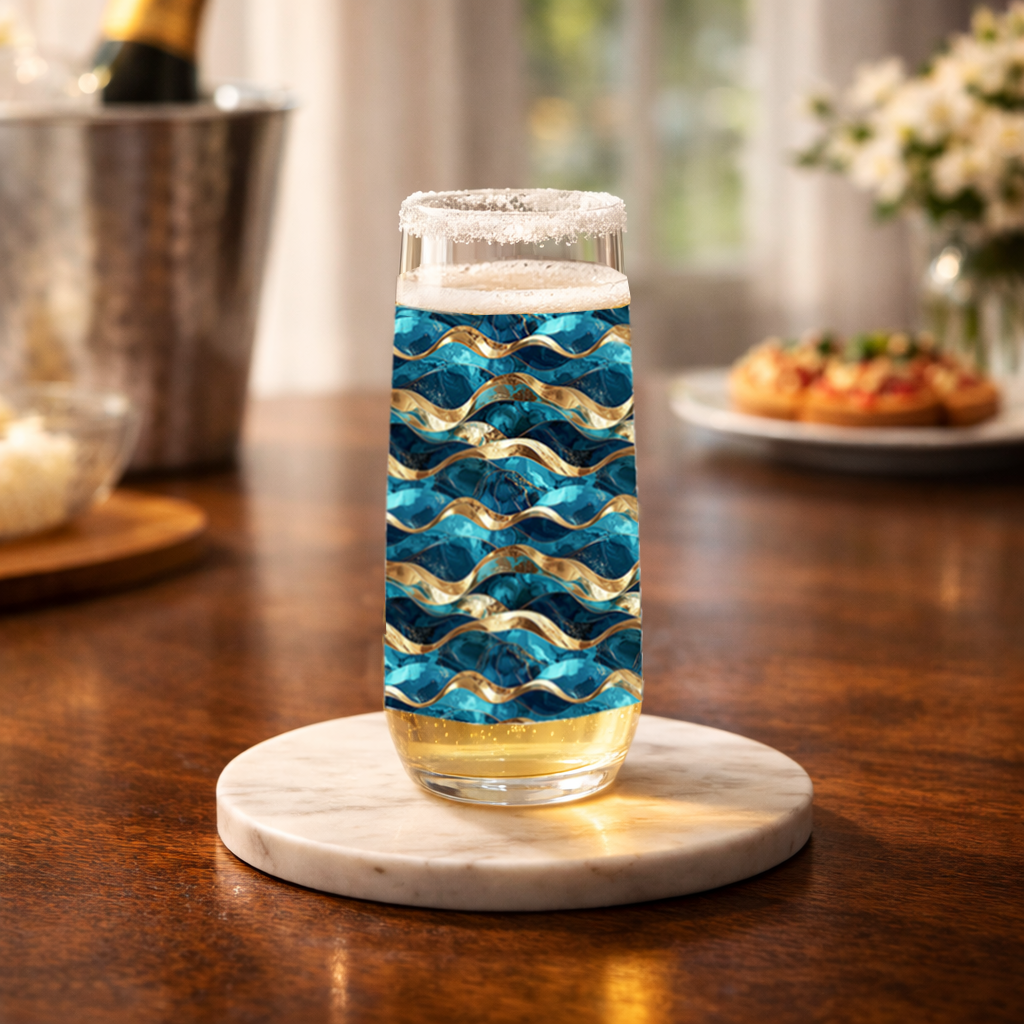 Opulent Teal stemless champagne flute glass with teal and gold decorative pattern on a table with champagne bucket and muffins blurred in background