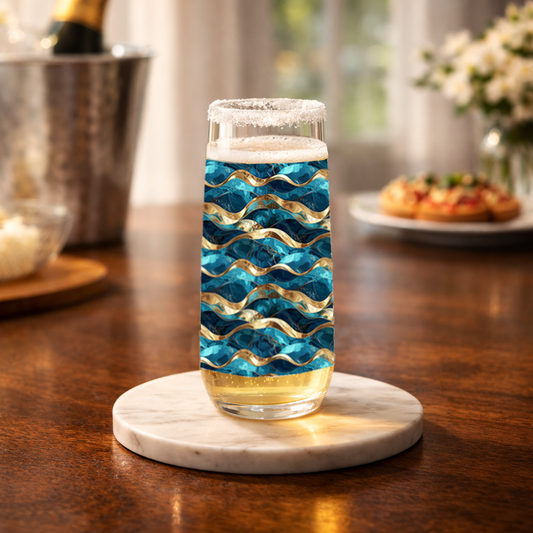 Opulent Teal stemless champagne flute glass with teal and gold decorative pattern on a table with champagne bucket and muffins blurred in background