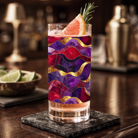 Fluid Marble highball glass with purple and gold design filled with a cocktail on ice and garnish, on a wooden table with a blurred background.