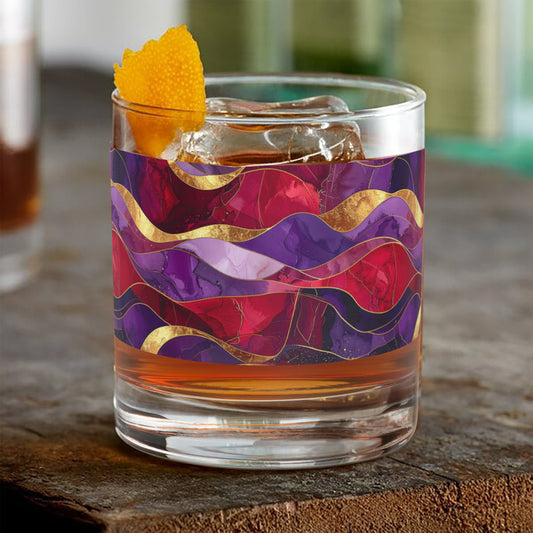 Fluid Marble signature rocks glass with purple and gold pattern filled with a cocktail and orange garnish on a wooden surface