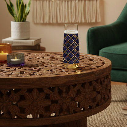 Regal Twilight stemless champagne glass with sapphire and gold wrap design on a wooden table in a cozy living room.