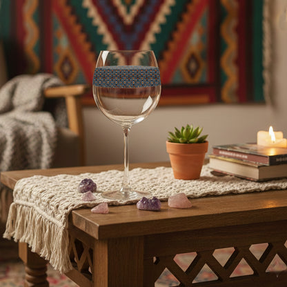 Burnished Slate balloon wine glass with a slate blue and copper design on a wooden table with candles, against a colorful tapestry background.