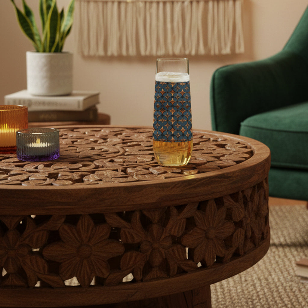 Burnished Slate stemless champagne glass with a slate blue and copper design and on a wooden table in a cozy room. 