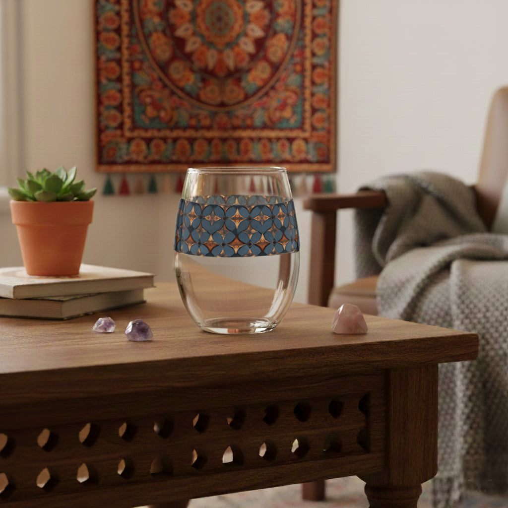 Burnished Slate stemless wine glass with slate blue and copper geometric pattern on a wooden table in a cozy living room.