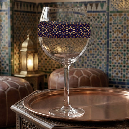 Midnight Marrakech balloon wine glass with a violet and gold design and sitting on a metallic tray with a tile wall in the background