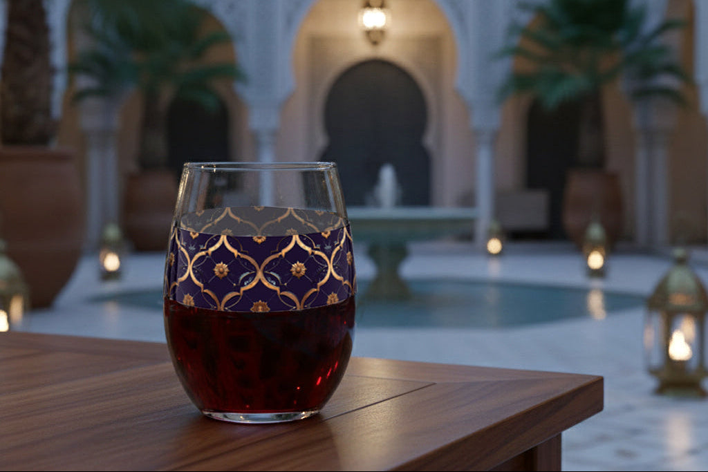 Midnight Marrakech stemless wine glass with a violet and gold design, sitting on a wooden table in an outdoor setting with Moroccan architectural elements and lanterns.